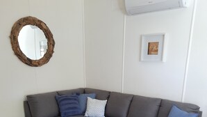 A living room with a grey sofa, a wooden coffee table, a small potted plant, and a decorative mirror on the wall. - Blue Haven - Pet friendly Cottage  (Iluka)