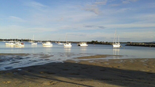 A beach with boats anchored in calm water, a sandy shore, and a distant shoreline with trees. - Blue Haven - Pet friendly Cottage  (Iluka)