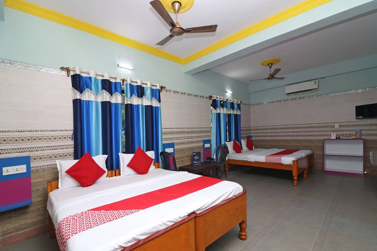 Habitación de hotel con dos camas de madera, cortinas azules, un ventilador de techo y un televisor en la pared.