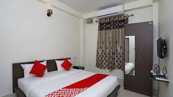 A hotel room with a bed, a wardrobe, a mirror, a TV, and an air conditioning unit.