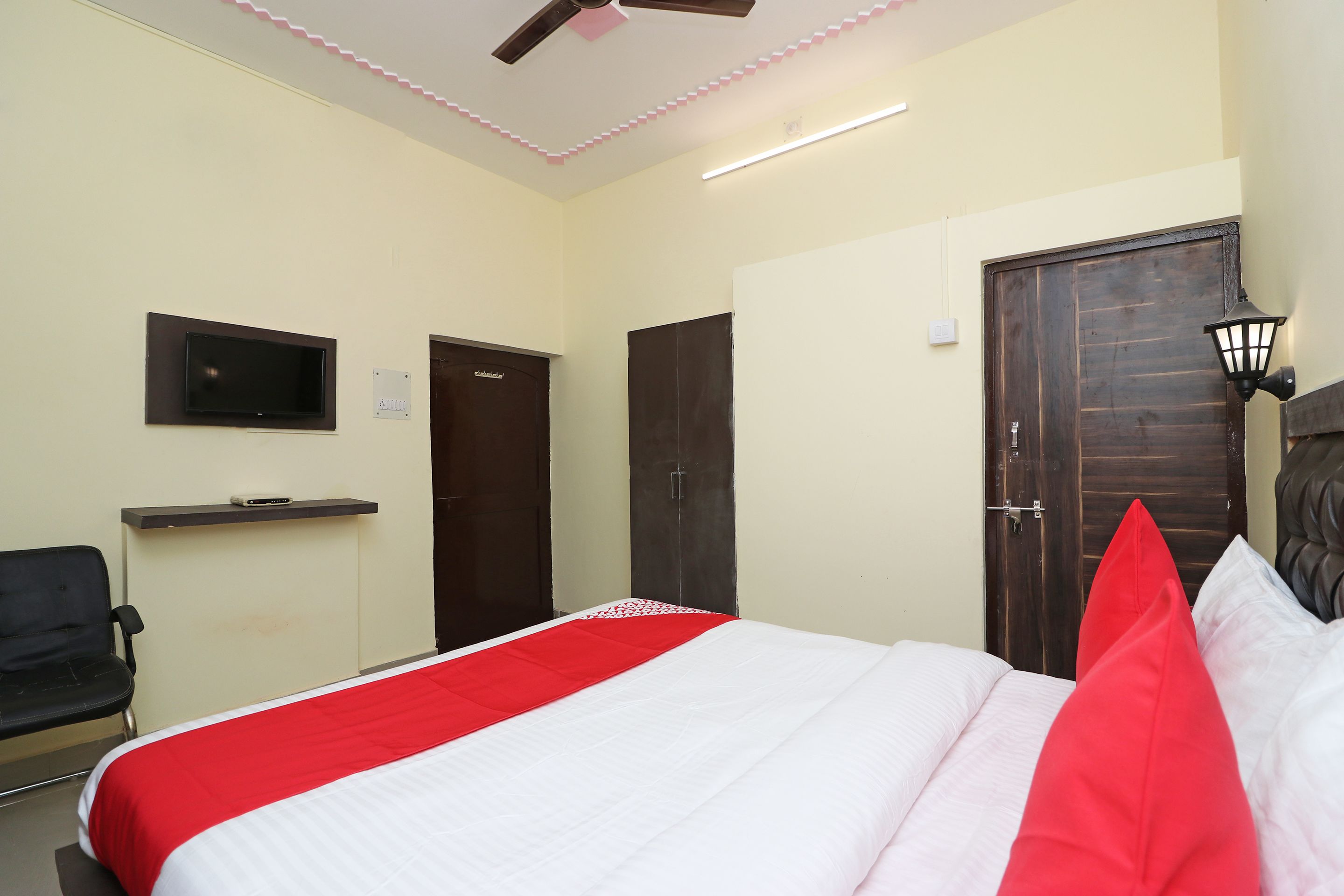 A hotel room with a bed, a TV mounted on the wall, a desk with a chair, and a door.