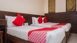 A hotel room with two beds, each with white bedding and red accents. There are wooden headboards and a nightstand with a lamp. - OYO 23656 Parimeet Hotel (Navi Mumbai)
