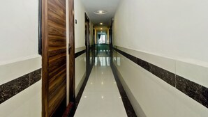 A long, narrow hallway with a polished floor, wooden doors, and a modern design. - OYO 23656 Parimeet Hotel (Navi Mumbai)