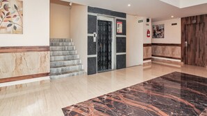 Un hall d’entrée moderne avec un sol en marbre, un escalier, une porte noire et une porte en bois.