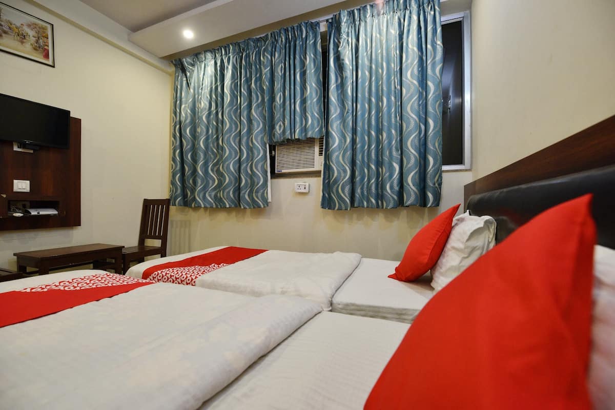 Ein Hotelzimmer mit zwei Betten, roter und weißer Bettwäsche, einem Holz-Kopfteil, einem an der Wand montierten Fernseher und einem Fenster mit gemusterten Vorhängen.