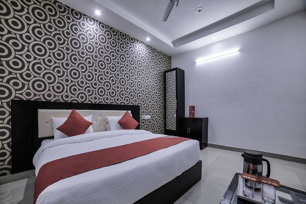 Una habitación de hotel moderna con una cama grande, un muro con estampado blanco y negro, un mueble negro y una cafetera sobre una mesa.