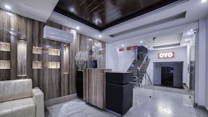 A modern reception area with a marble floor, a reception desk, a white sofa, and a staircase leading to an upper level.