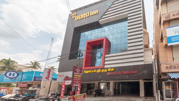 A hotel with a prominent 'GURU INN' sign, a large glass facade, and a 'SALE' sign visible in front. - OYO 19909 Sri Guru Inn (Coimbatore)
