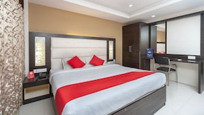 A modern hotel room with a large bed, a desk, and a ceiling fan. - OYO 19909 Sri Guru Inn (Coimbatore)