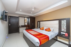 A hotel room with a large bed, a bedside table with a phone and a red card, a ceiling fan, and a TV mounted on the wall. - OYO 19909 Sri Guru Inn (Coimbatore)