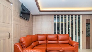 A modern living room with a sectional sofa, wooden panel walls, a flat-screen TV, and a glass partition with vertical blinds.