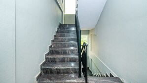 Una escalera con escalones de mármol oscuro y barandilla negra, que conduce a una habitación luminosa con ventanal.