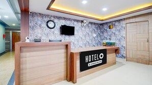 Un mostrador de recepción de hotel con una pared con diseño de mármol, un reloj y un televisor.