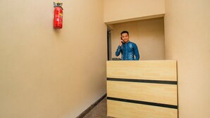 Un passadís d'hotel amb un taulell de recepció de fusta, un extintor fixat a la paret i una persona al darrere del taulell.