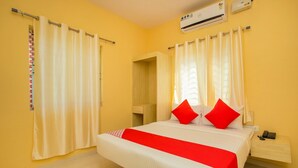 Habitació d'hotel amb un llit, cortines, un aparell d'aire condicionat, una taula de nit amb un telèfon i un petit mirall.