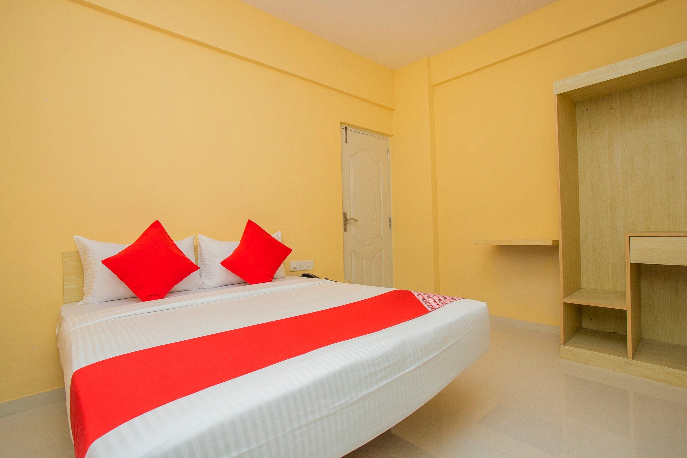 A neatly made bed with white and red bedding, a wooden wardrobe, and a plain yellow wall.