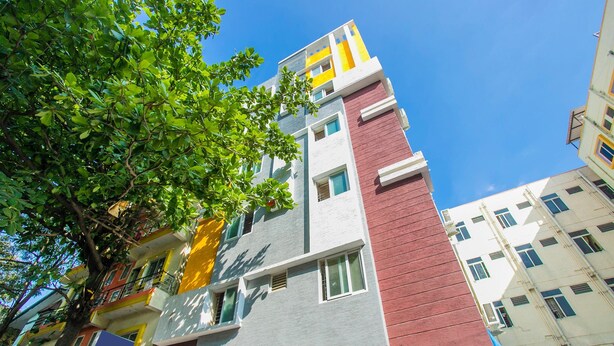Edifici d'altes plantes amb façana que combina murs de color vermell, groc i gris, balcons i finestres.