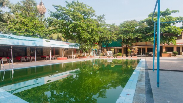 A swimming pool with a tiled edge, surrounded by trees and a building with a sign that reads "VORRESORT". - OYO 12693 Manori Resort (Gorai)