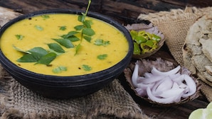 A bowl of yellow soup garnished with herbs, accompanied by sliced onions, green chilies, and a lime half on a rustic wooden table. - OYO 12693 Manori Resort (Gorai)