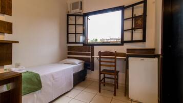 Una habitación pequeña y funcional con una cama individual, un escritorio, una silla y un refrigerador.