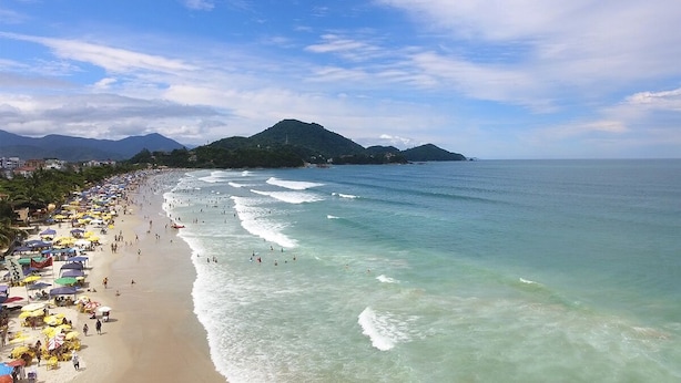 Ein Strand mit klarem Wasser, Sonnenschirmen und einem Berg im Hintergrund.