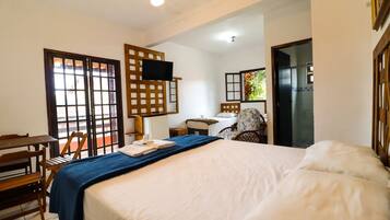 Habitación de hotel con cama, escritorio, silla, televisor y ventana con vista a vegetación.
