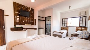 Ein Hotelzimmer mit einem großen Bett, einem an einer Holzplatte montierten Fernseher, einem kleinen Tisch mit einem Stuhl und einem Fenster mit Jalousien.