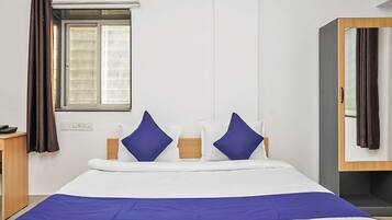 A hotel room with a bed, a window with curtains, a bedside table, and a wardrobe.