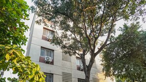 A multi-story building with air conditioning units on the windows, surrounded by trees and flowering plants. - OYO 19530 SilverKey Vishrantwadi (Pune)