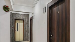 A hallway with a marble wall, a wooden door, and a wall-mounted light switch. - OYO 19530 SilverKey Vishrantwadi (Pune)