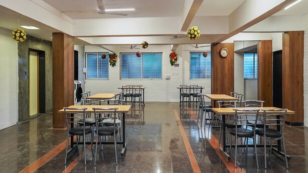 A spacious conference room with multiple tables and chairs, large windows, and ceiling fans. - OYO 19530 SilverKey Vishrantwadi (Pune)