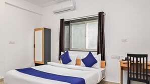 A hotel room with a bed, a desk, a chair, an air conditioning unit, and a window with curtains. - OYO 19530 SilverKey Vishrantwadi (Pune)
