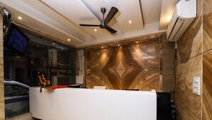 A reception desk with a modern design, a ceiling fan, and an air conditioning unit on the wall. - OYO 24677 Tashkent (New Delhi)