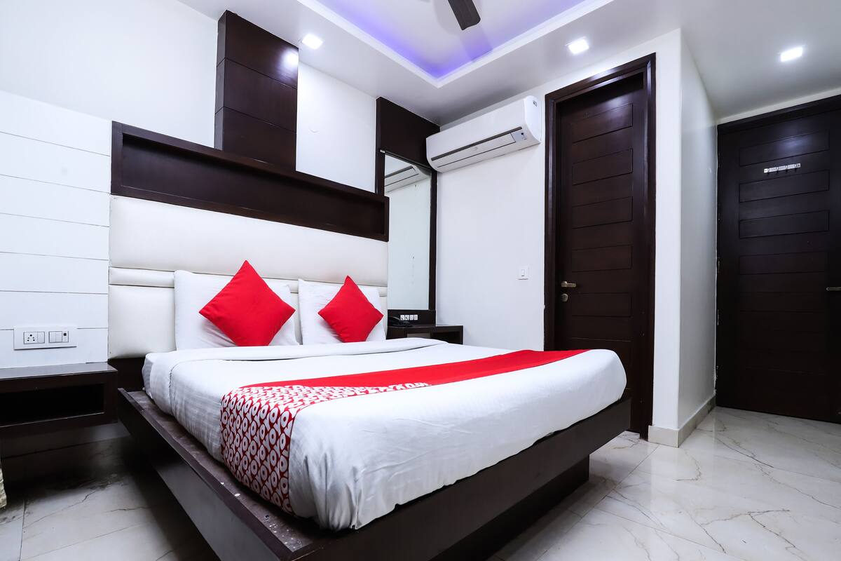 Un dormitorio moderno con una cama grande, ropa de cama blanca y roja, un cabecero oscuro e iluminación empotrada en el techo.