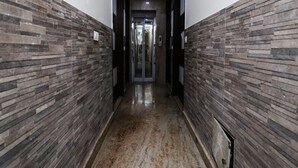 A hallway with stone-patterned walls and a polished floor, leading to a door with a glass panel. - OYO 24677 Tashkent (New Delhi)