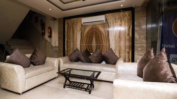 A hotel lobby with a modern design, featuring a sofa set, a glass coffee table, and a ceiling fan.