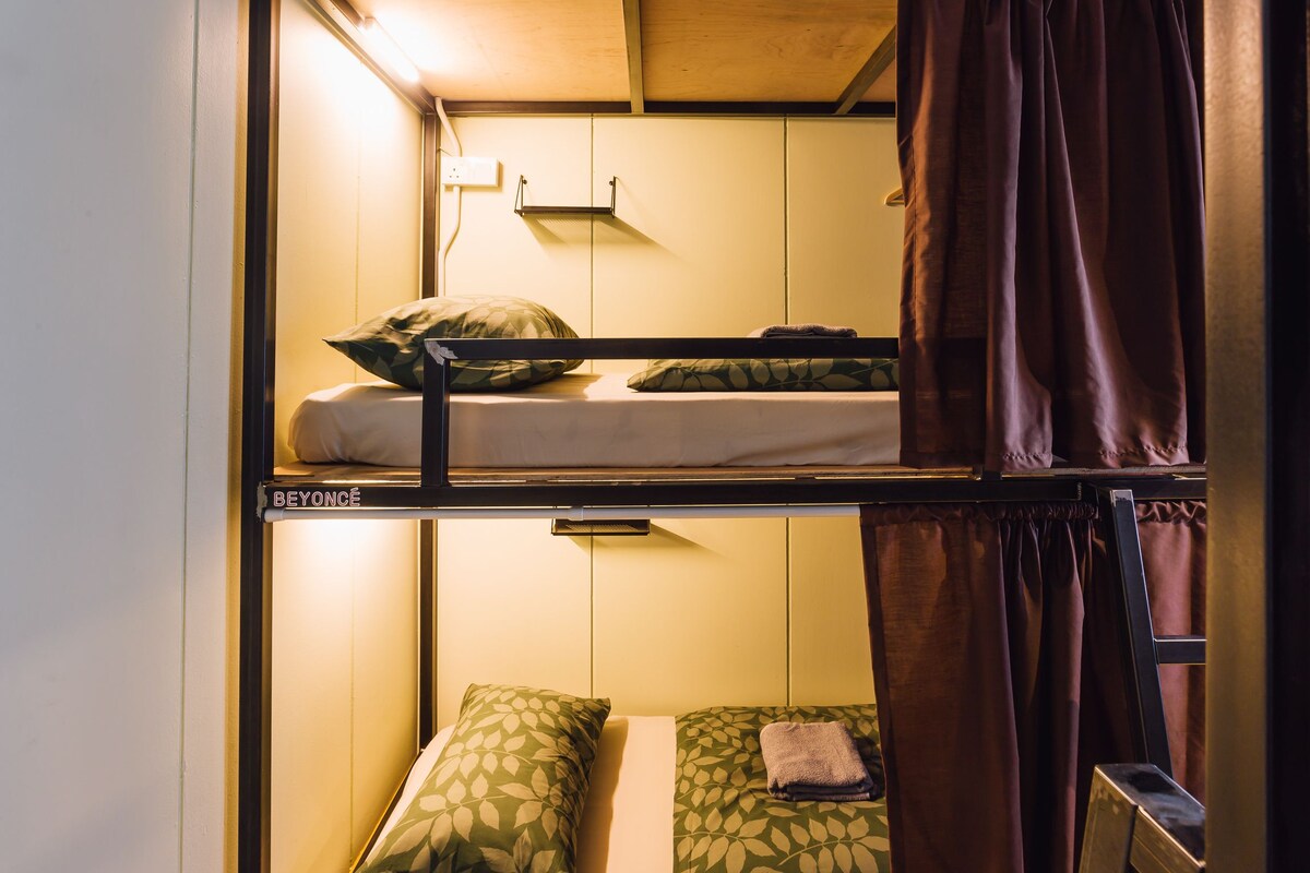 A bunk bed room with a shelf above the upper bunk and a small table with a towel on the lower bunk.