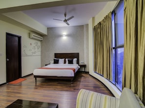A hotel room with a large bed, a ceiling fan, a nightstand, and a window with curtains.