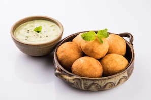 A bowl of golden-brown fried balls with a mint garnish and a bowl of green dip.