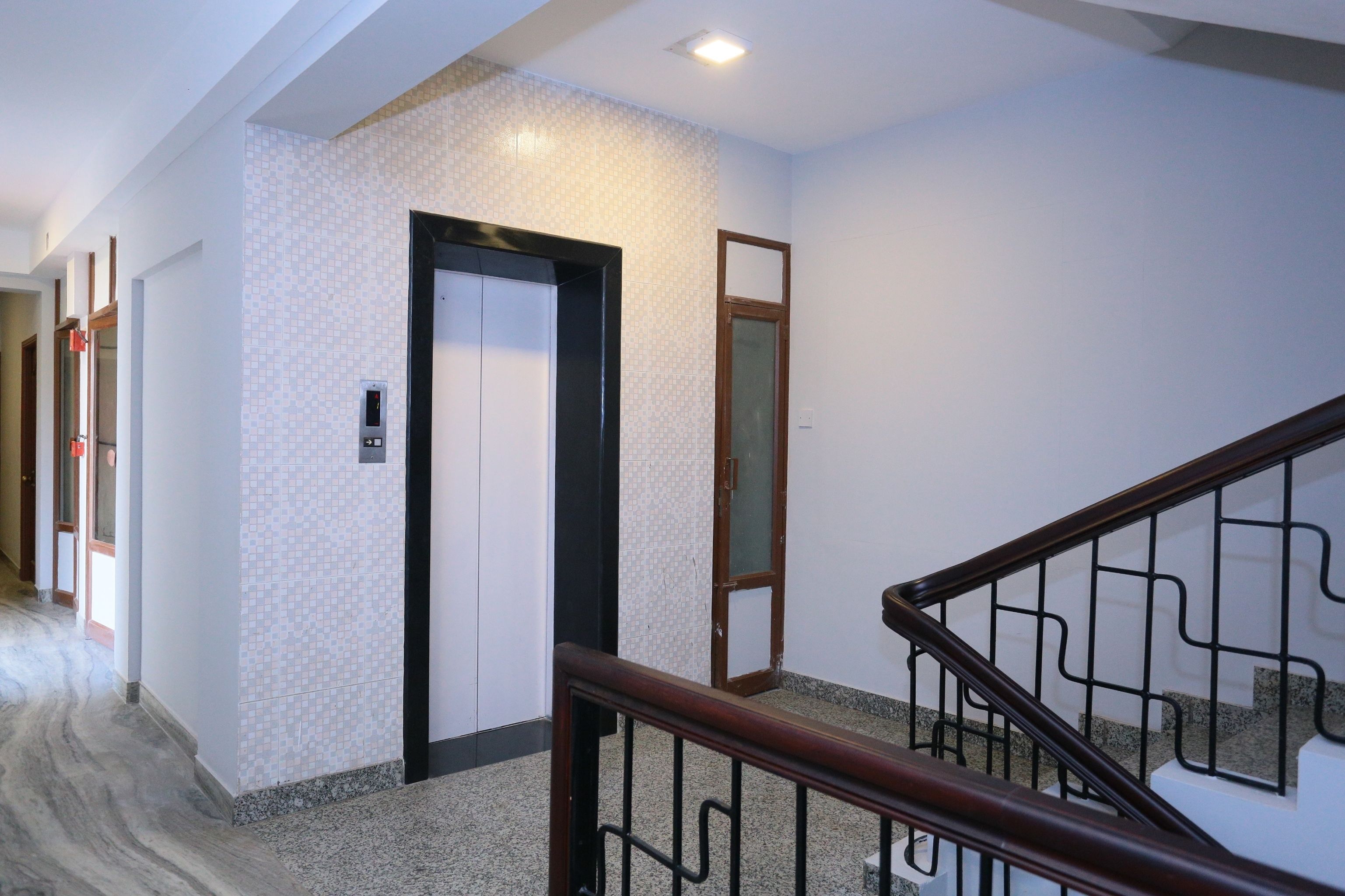 A hallway with a marble floor, a wooden staircase with metal railings, and a door with a small elevator panel.