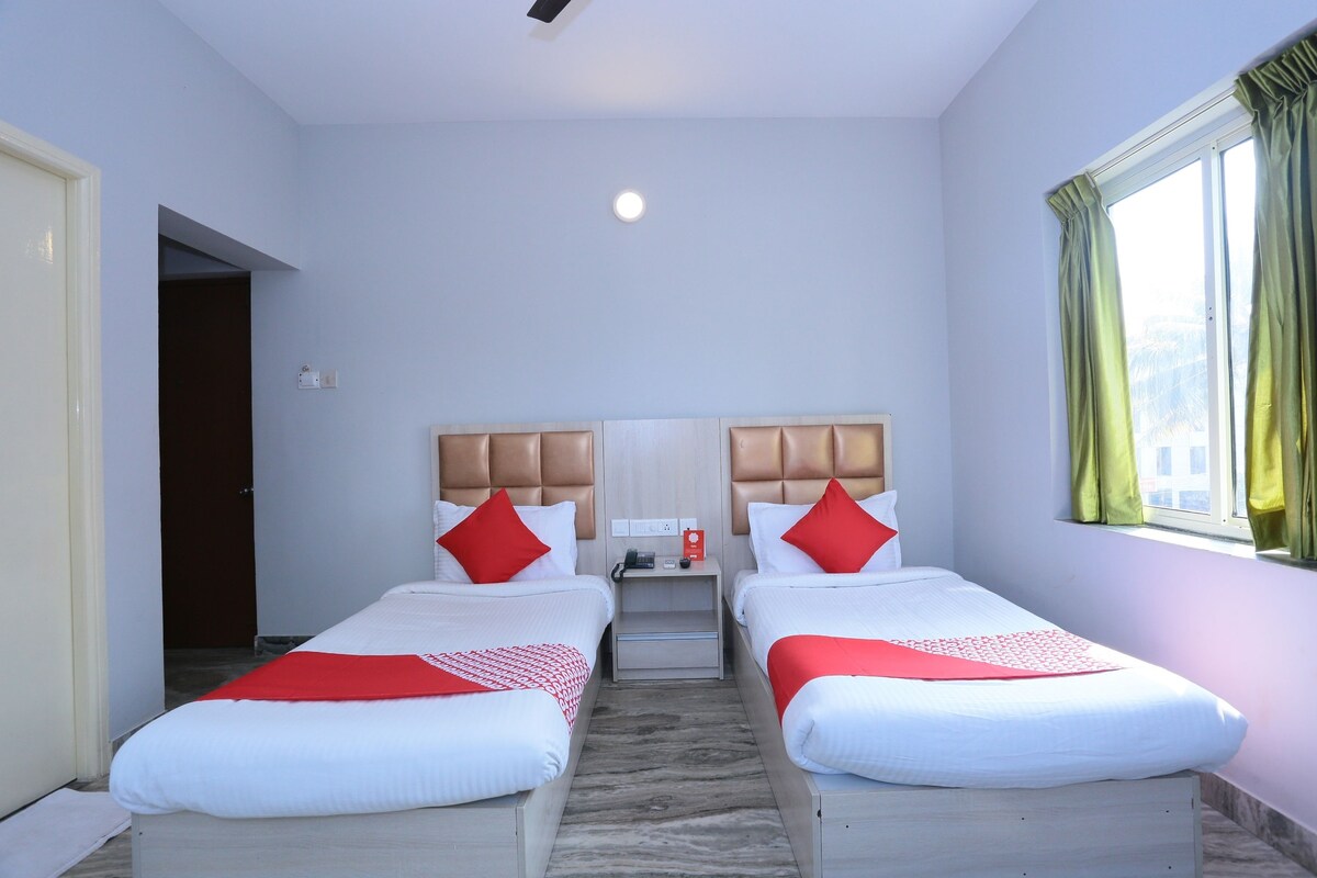 A hotel room with two beds, a nightstand, a window with curtains, and a door.