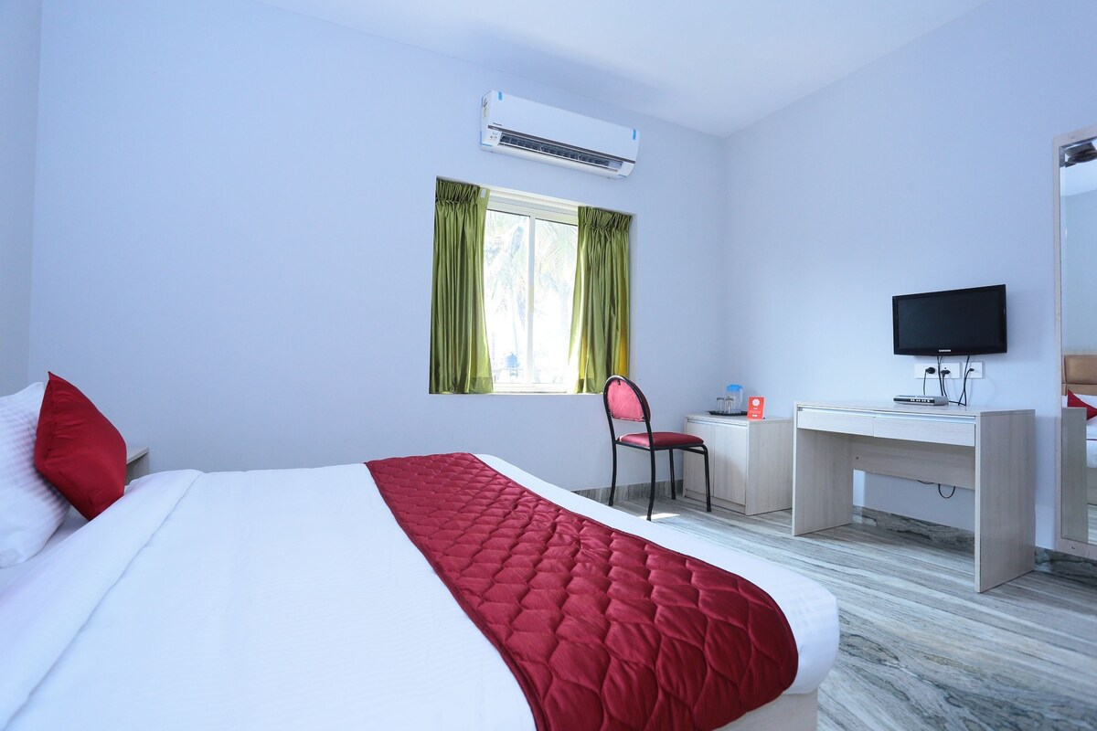 A hotel room with a bed, a desk, a chair, a TV, and an air conditioning unit.