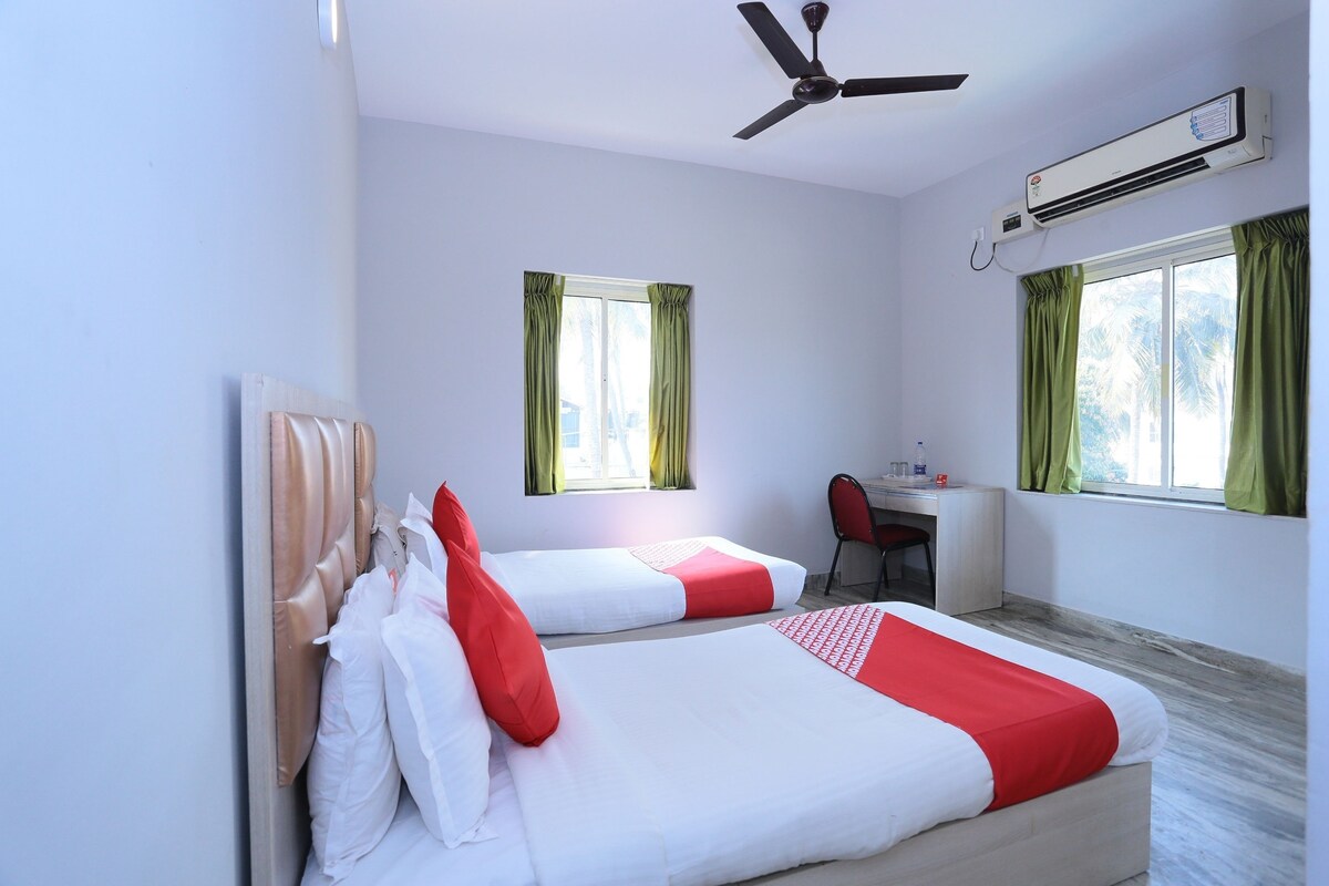 A hotel room with two beds, a desk, a chair, a ceiling fan, and an air conditioning unit.
