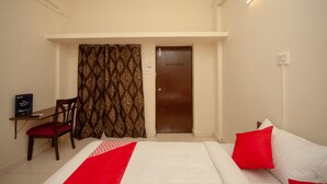 Ein Hotelzimmer mit Bett, Schreibtisch, Stuhl, Tür und Vorhängen.