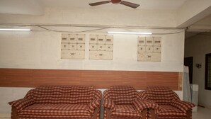 Ein Zimmer mit zwei gemusterten Sofas, einem Deckenventilator, Neonleuchten und elektrischen Schaltkästen an der Wand.