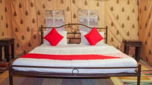 Ein Bett mit weißer Matratze und roten Kissen, ein Holz-Kopfbrett und ein Fenster mit Vorhängen.