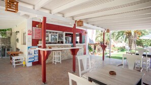 An outdoor cafe with white tables and chairs, a red counter, and a stone-tiled floor. - Helena Inn (Kefalonia)