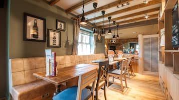 A wooden dining area with a bench and chairs, framed pictures on the wall, and a kitchen visible in the background.