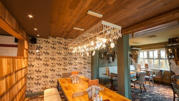 A restaurant interior with wooden ceiling, patterned wallpaper, and a long wooden table with menu stands.