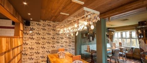 A restaurant interior with wooden ceiling, patterned wallpaper, and a long wooden table with menu stands.